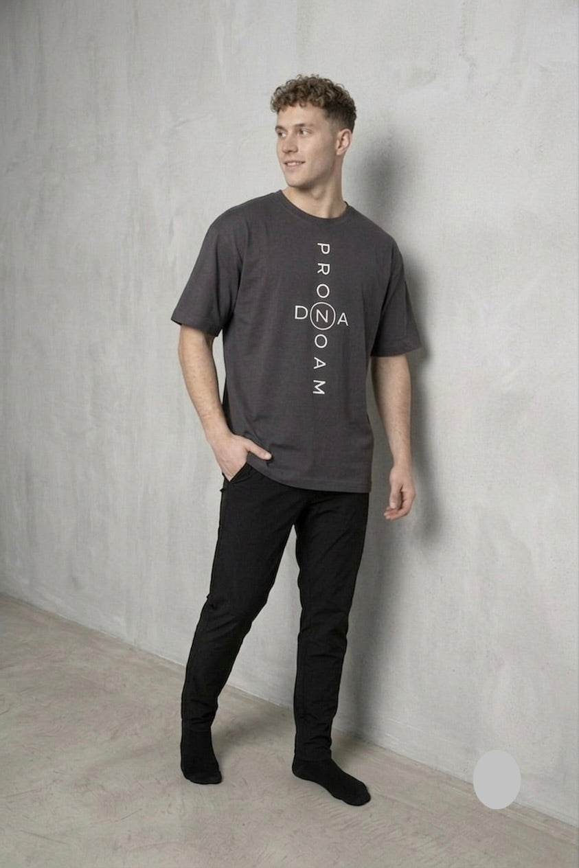 Men’s minimalist dark grey PRONOAM T‑shirt in oversized fit, clean luxury streetwear aesthetic, styled with black tapered trousers in a neutral concrete interior for e‑commerce fashion display. Premium men’s charcoal grey PRONOAM T‑shirt featuring bold vertical PRONOAM branding with circled Z/N emblem, modern streetwear silhouette, paired with black slim trousers against a minimalist concrete backdrop. Men’s dark grey oversized PRONOAM T‑shirt with vertical white PRONOAM DNA branding, minimalist street‑lux